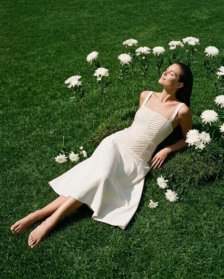 Model in a cream corset midi dress lying on the grass among white daisies